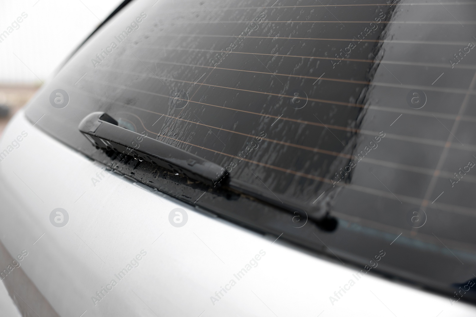 Photo of Wiper cleaning raindrops from car rear windshield outdoors