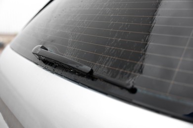Wiper cleaning raindrops from car rear windshield outdoors