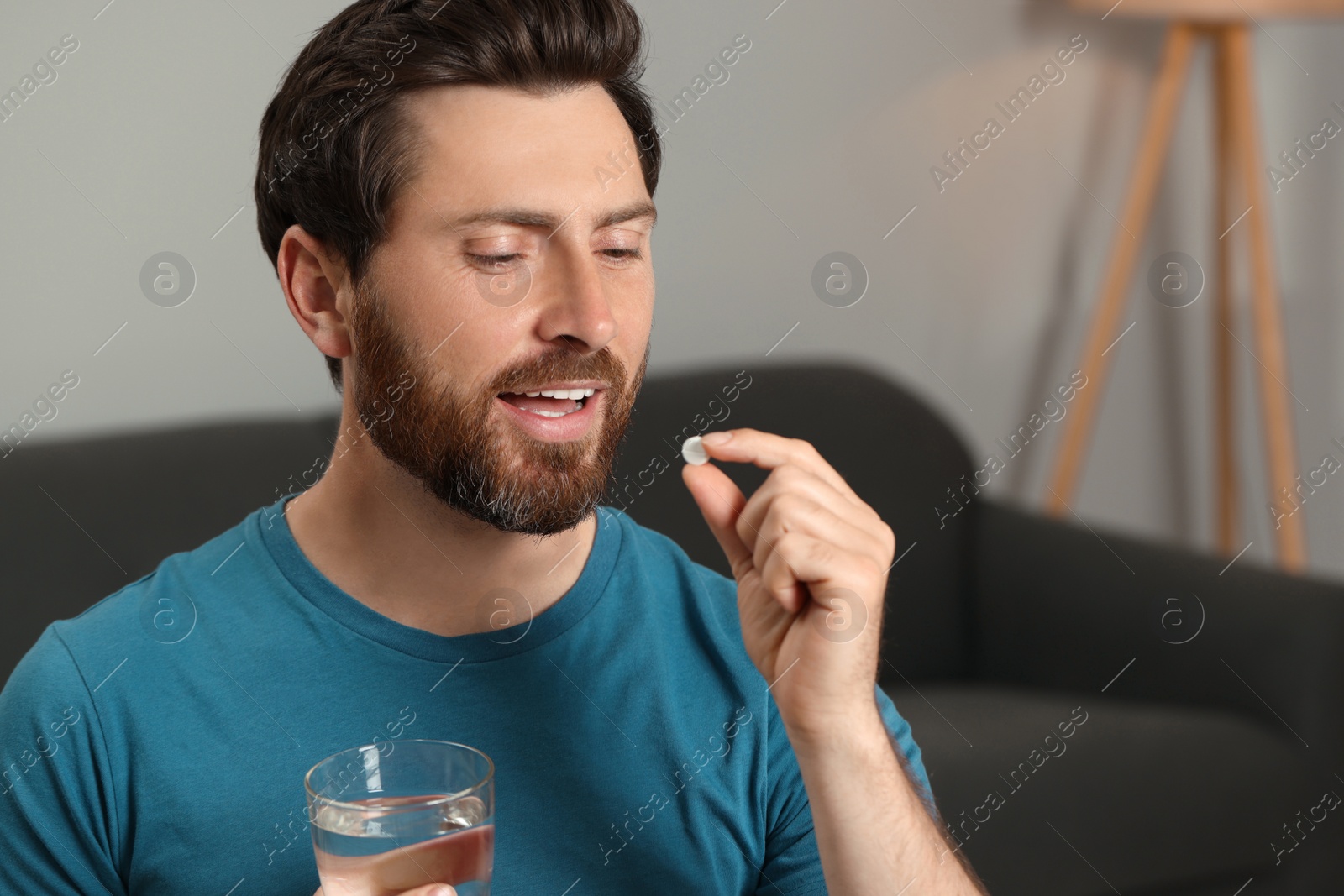 Photo of Handsome man with glass of water taking pill at home, space for text