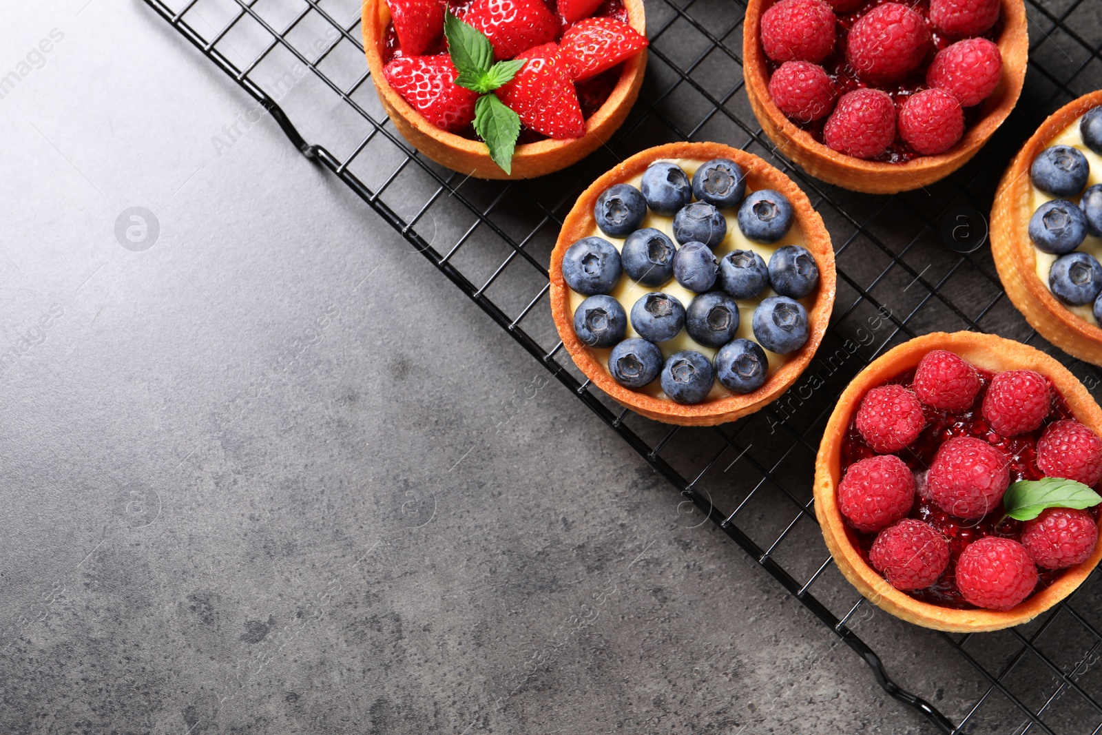 Photo of Tartlets with different fresh berries on grey table, top view and space for text. Delicious dessert