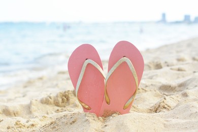 Photo of Stylish flip flops in sand on beach near sea