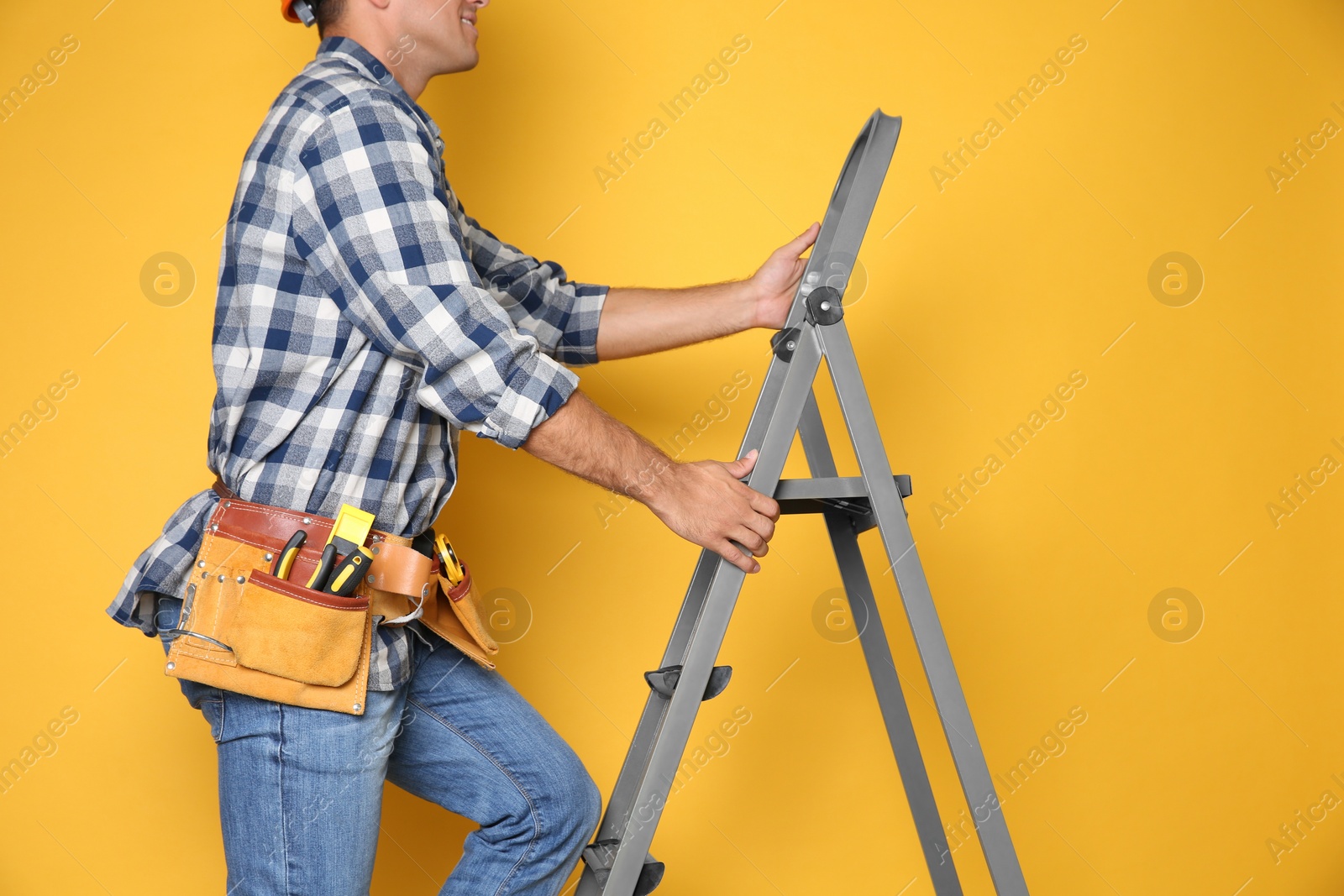 Photo of Professional builder climbing up metal ladder on yellow background, closeup