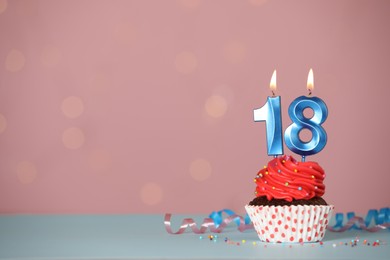 Photo of Coming of age party - 18th birthday. Delicious cupcake with number shaped candles on light blue table, space for text