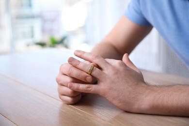 Photo of Man taking off wedding ring at wooden table indoors, closeup. Divorce concept