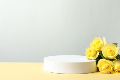 Photo of Beautiful presentation for product. Round podium and yellow roses on beige table against light grey background, space for text