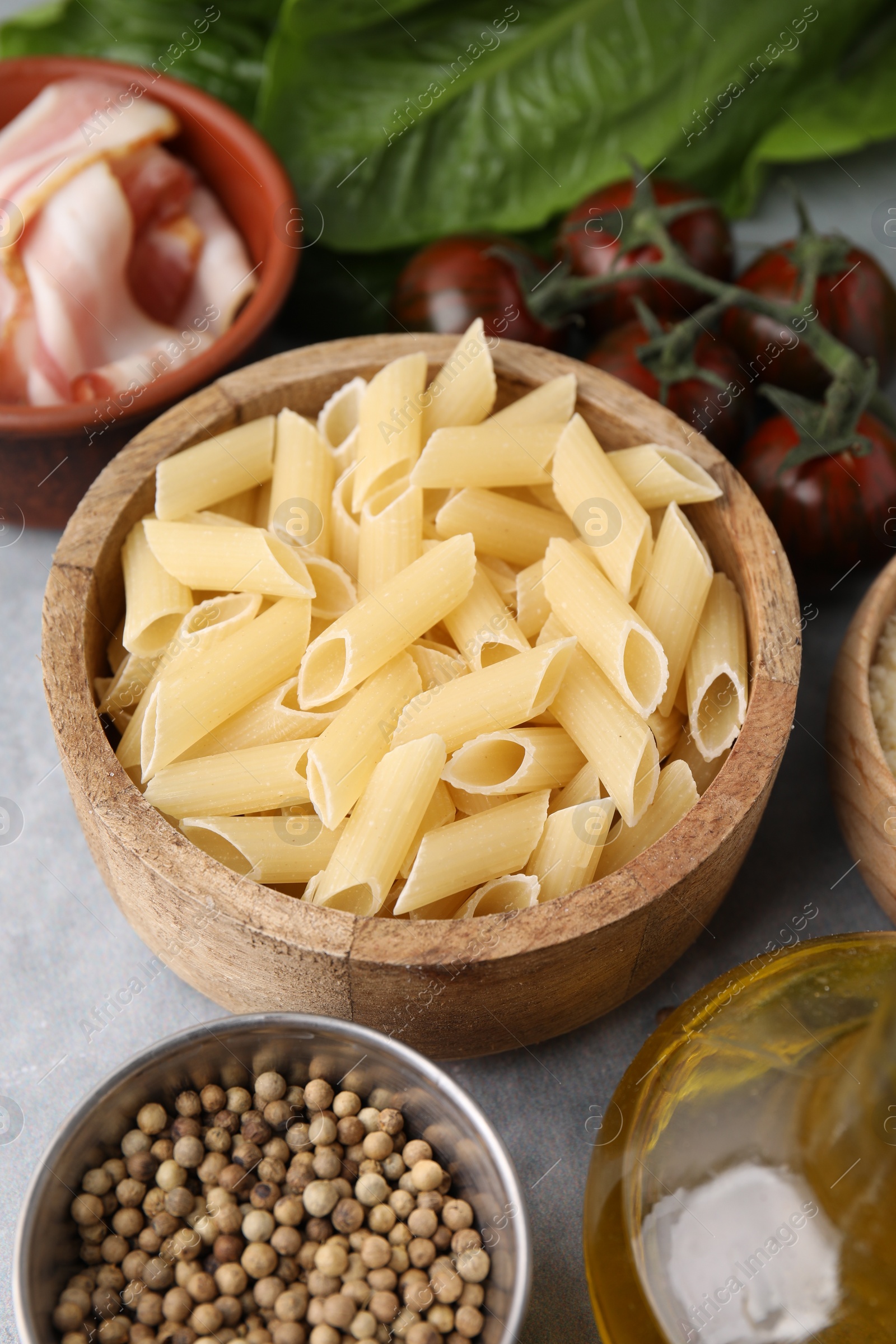 Photo of Raw pasta, bacon and fresh ingredients on light grey table