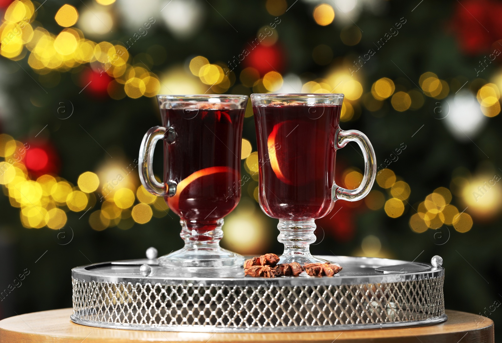 Photo of Hot mulled wine in glass cups and anise stars on table against blurred lights