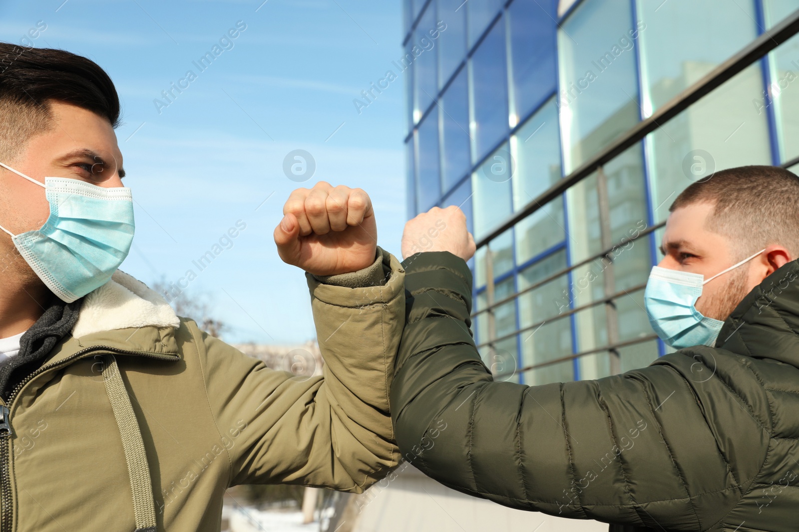 Photo of Men in masks greeting each other by bumping elbows outdoors