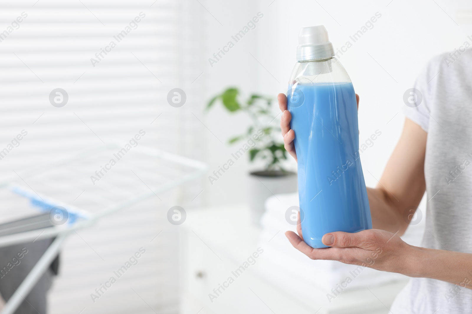 Photo of Woman holding fabric softener in bathroom, closeup. Space for text
