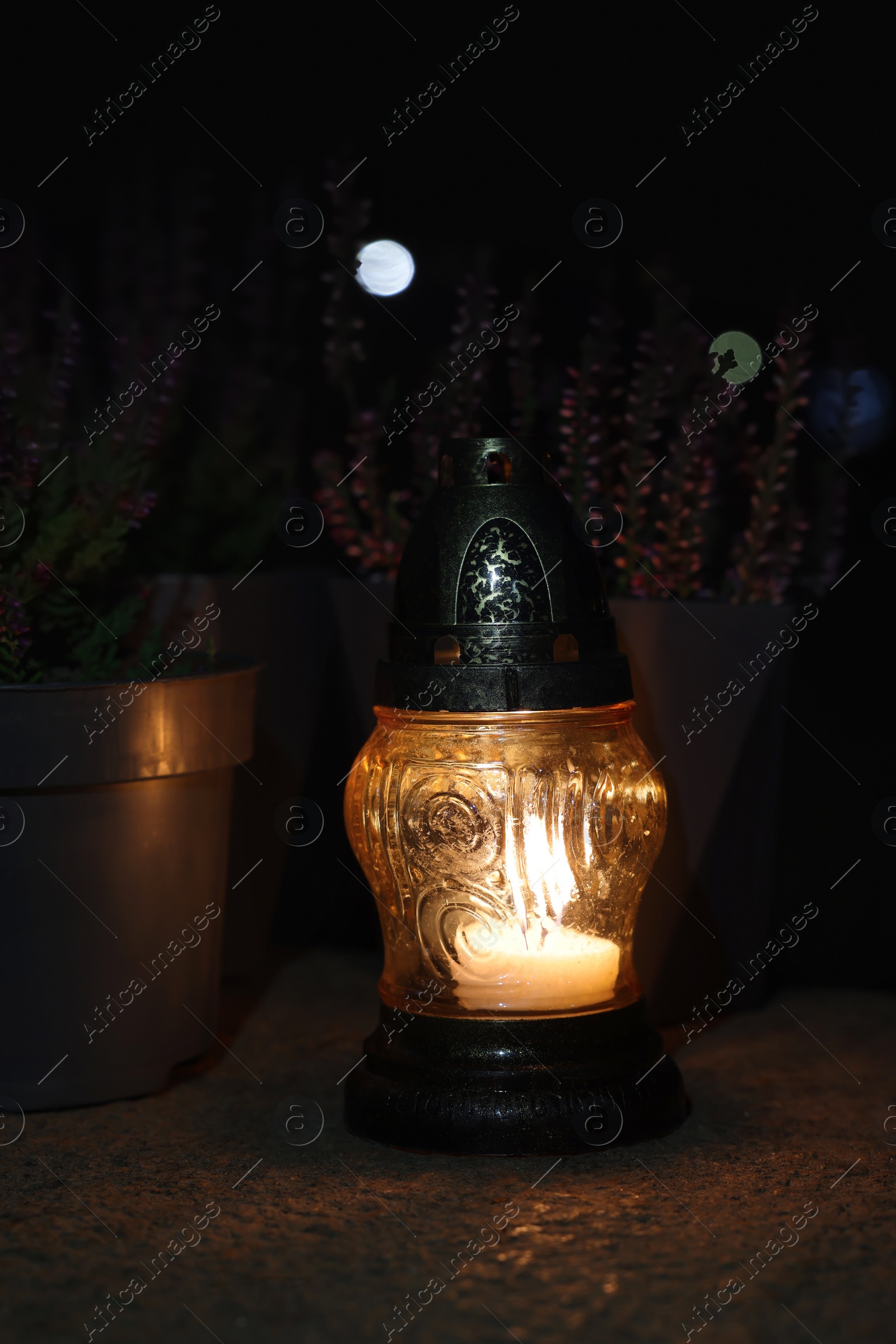 Photo of Grave lantern with burning candle on stone surface at night