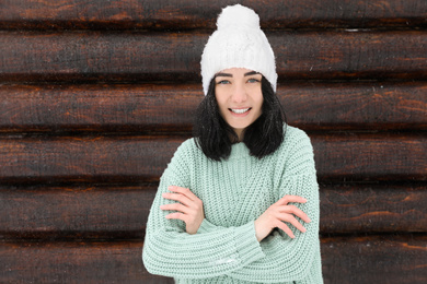 Photo of Young woman wearing warm sweater and hat near wooden wall. Winter season