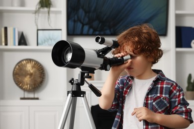 Photo of Cute little boy looking at stars through telescope in room
