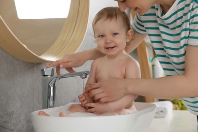 Mother washing her little baby in sink at home