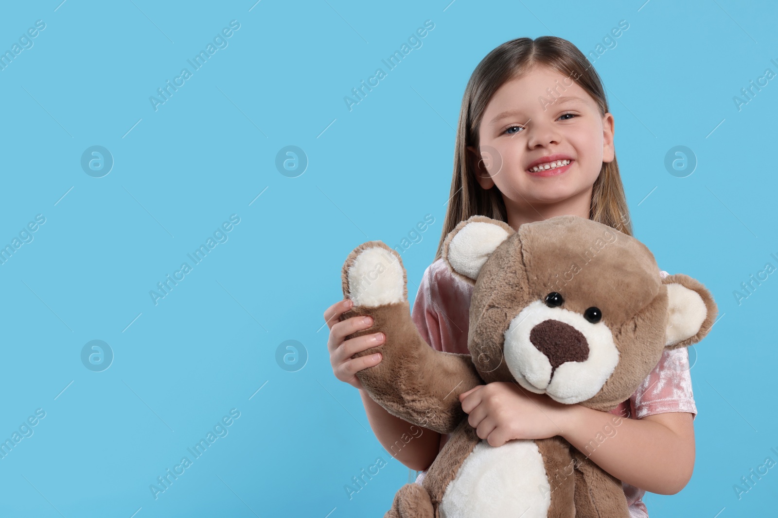 Photo of Cute little girl with teddy bear on light blue background. Space for text