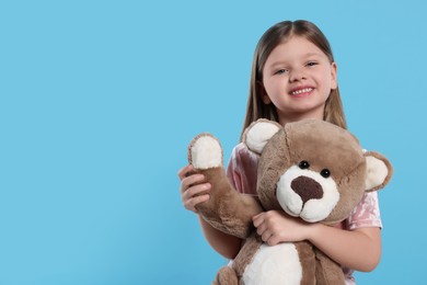 Photo of Cute little girl with teddy bear on light blue background. Space for text