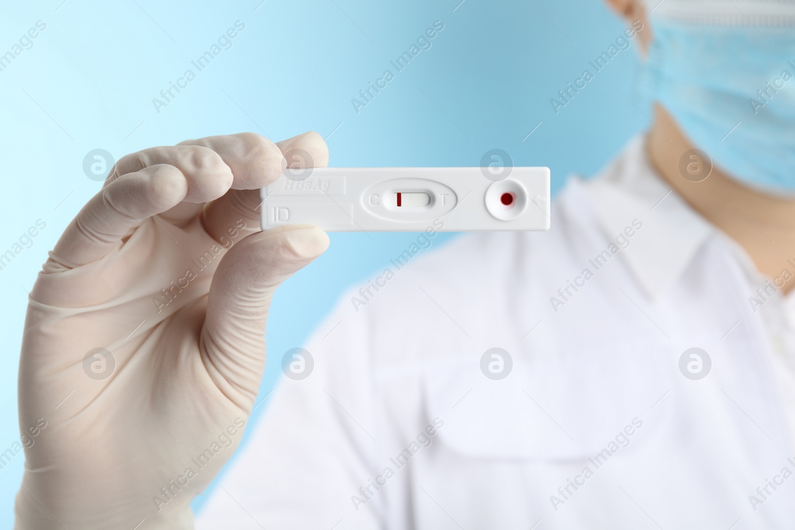 Photo of Doctor holding disposable express test for hepatitis on light blue background, closeup