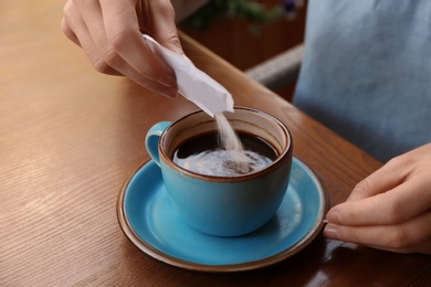 Photo of Woman adding sugar to fresh aromatic coffee at table, closeup