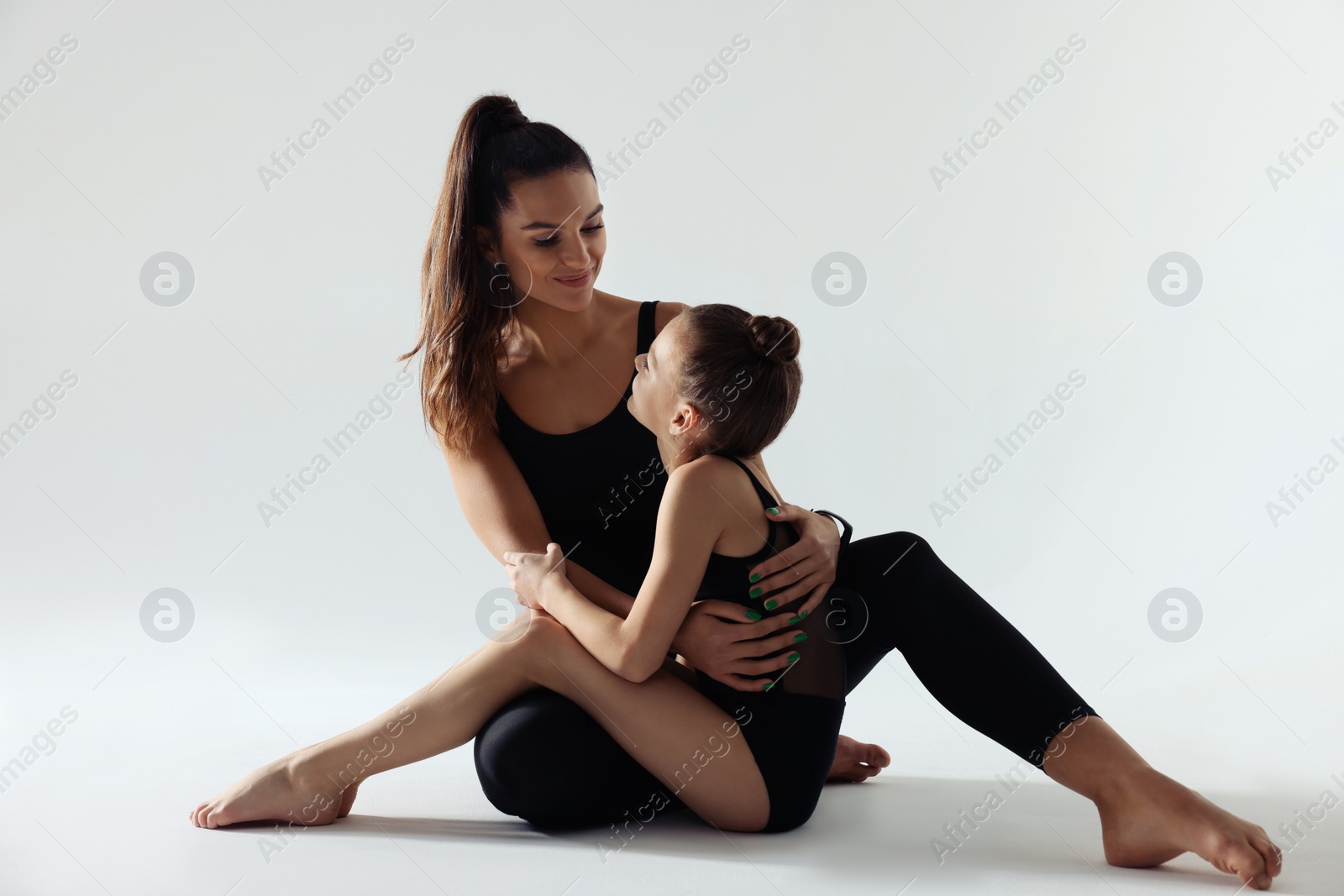 Photo of Little gymnast and her coach sitting on white background