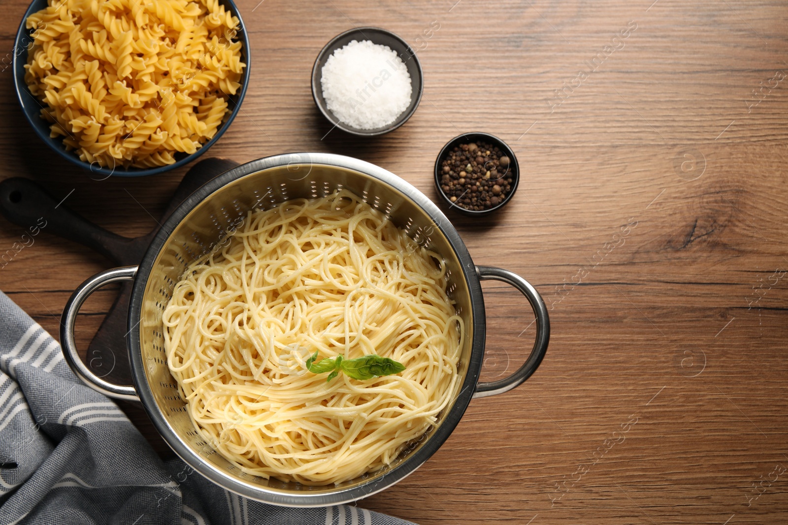 Photo of Cooked pasta in metal colander and spices on wooden table, flat lay. Space for text