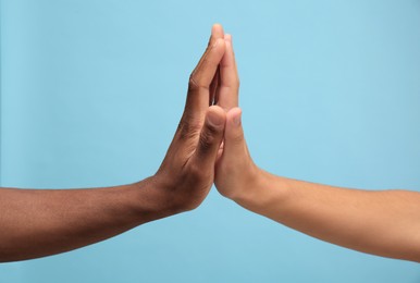 Photo of Men giving high five on light blue background, closeup