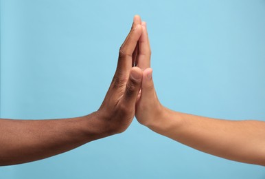 Men giving high five on light blue background, closeup