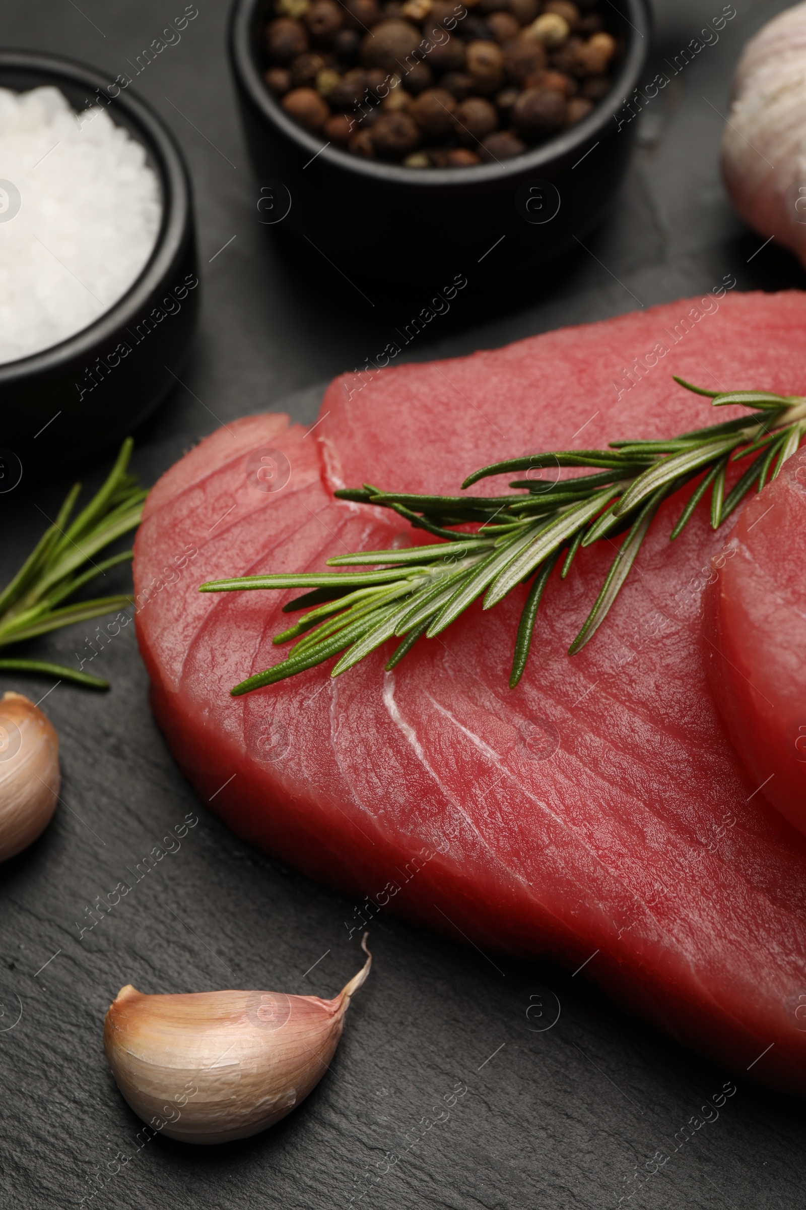 Photo of Fresh raw tuna fillet with rosemary and spices on black table