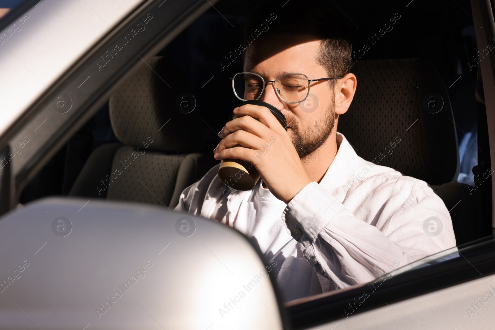 Photo of To-go drink. Handsome man drinking coffee in car