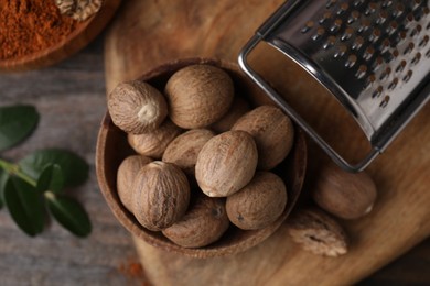 Photo of Nutmegs in bowl and grater on wooden table, flat lay
