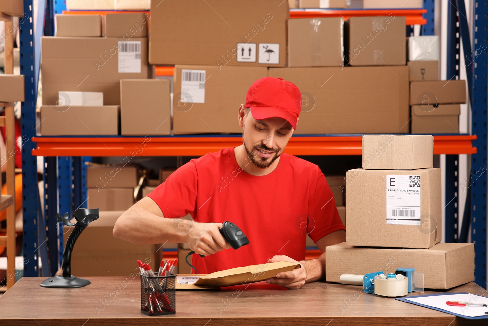 Photo of Post office worker with scanner reading parcel barcode at counter indoors