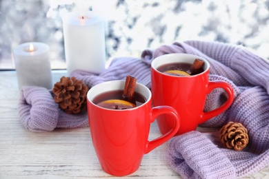 Photo of Cups of hot winter drink with knitted sweater on window sill indoors