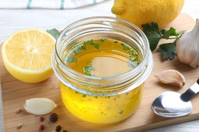 Photo of Jar with lemon sauce and ingredients on wooden board, closeup. Delicious salad dressing