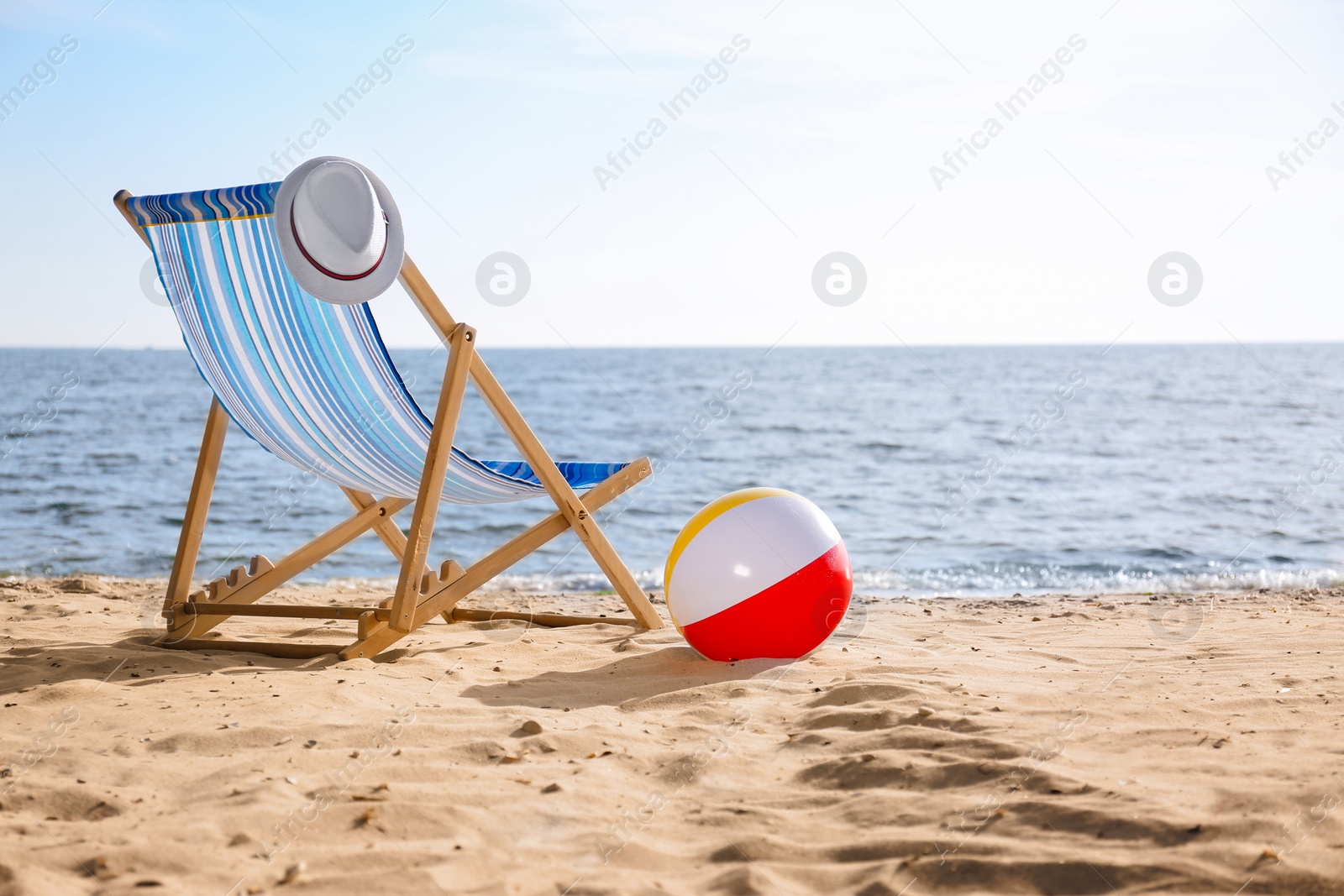 Photo of Lounger, hat and inflatable ball on sand near sea, space for text. Beach objects