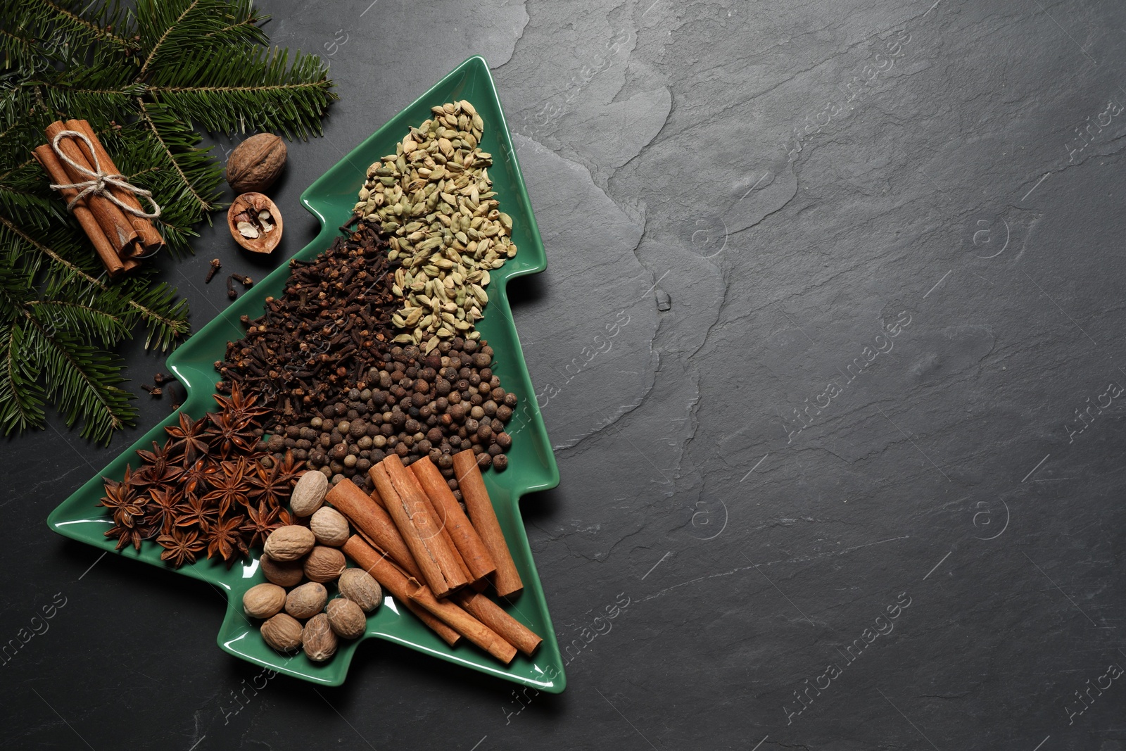 Photo of Different spices, nuts and fir branches on dark gray textured table, flat lay. Space for text