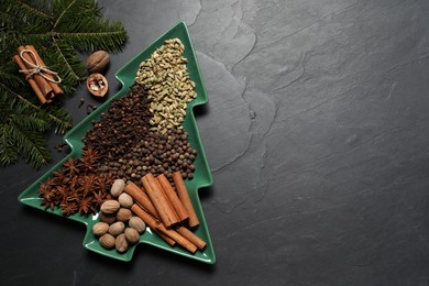 Different spices, nuts and fir branches on dark gray textured table, flat lay. Space for text