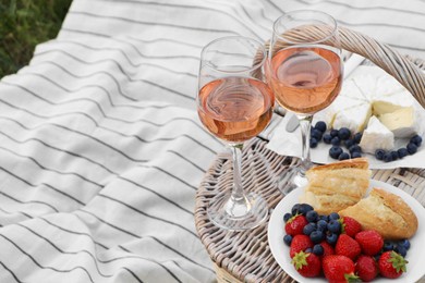 Photo of Glasses of delicious rose wine, food and basket on picnic blanket outdoors