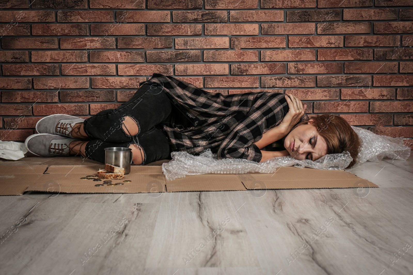 Photo of Poor homeless woman sleeping on floor near brick wall