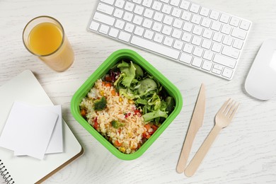 Photo of Container with tasty food, cutlery, keyboard, glass of juice and notebooks on white wooden table, flat lay. Business lunch
