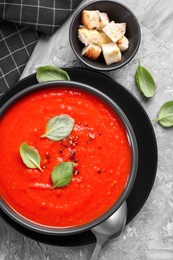 Photo of Delicious tomato cream soup served on grey textured table, flat lay