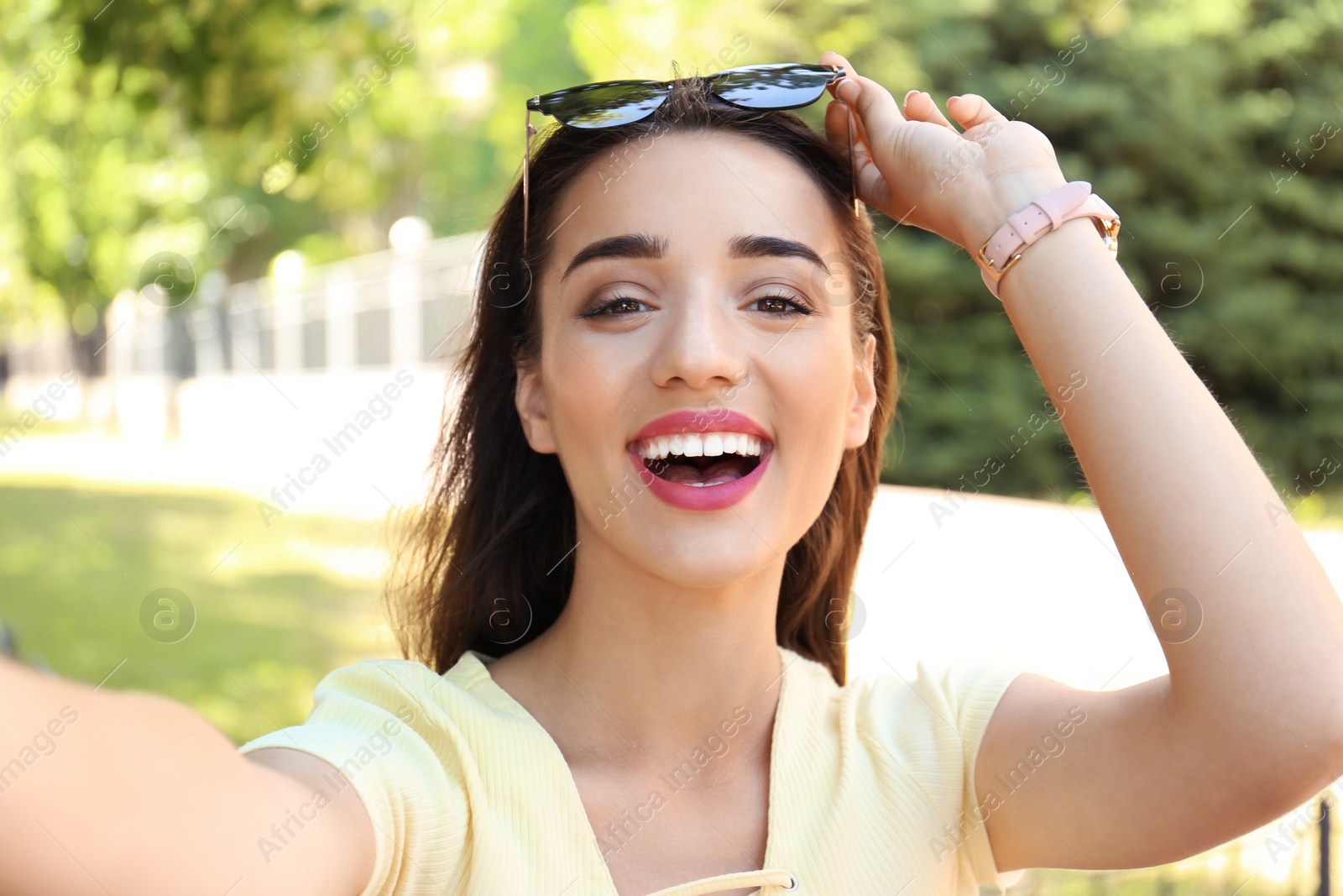 Photo of Young woman taking selfie outdoors on sunny day