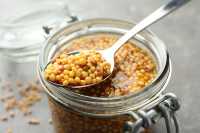 Photo of Whole grain mustard in jar and spoon on table, closeup