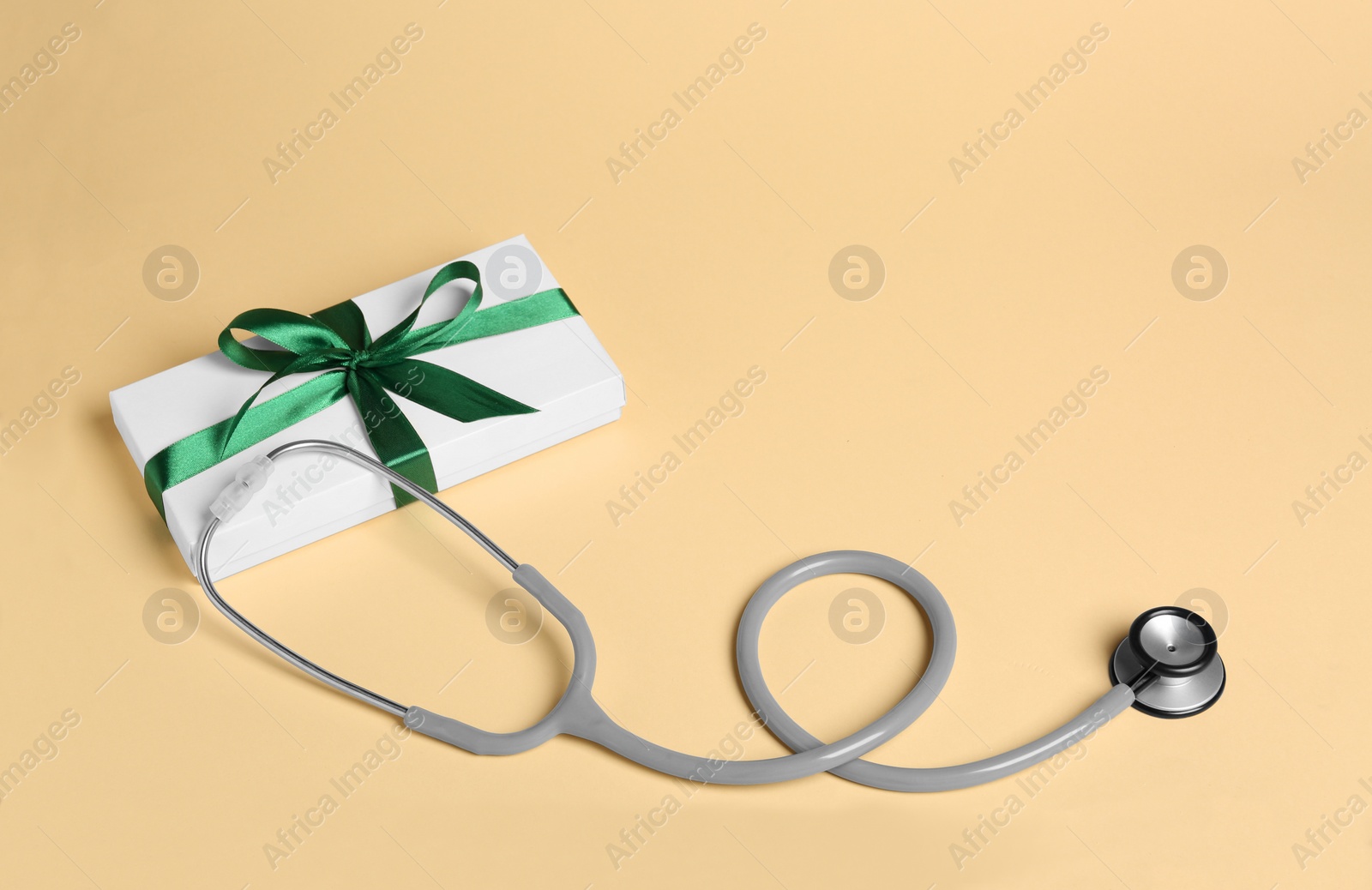 Photo of Stethoscope and gift box on beige background, space for text. Happy Doctor's Day