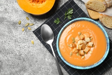 Photo of Tasty creamy pumpkin soup served with bread on grey table, flat lay. Space for text