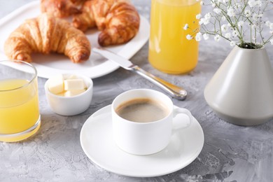 Photo of Tasty breakfast. Cup of coffee, butter and fresh croissants on grey table, closeup