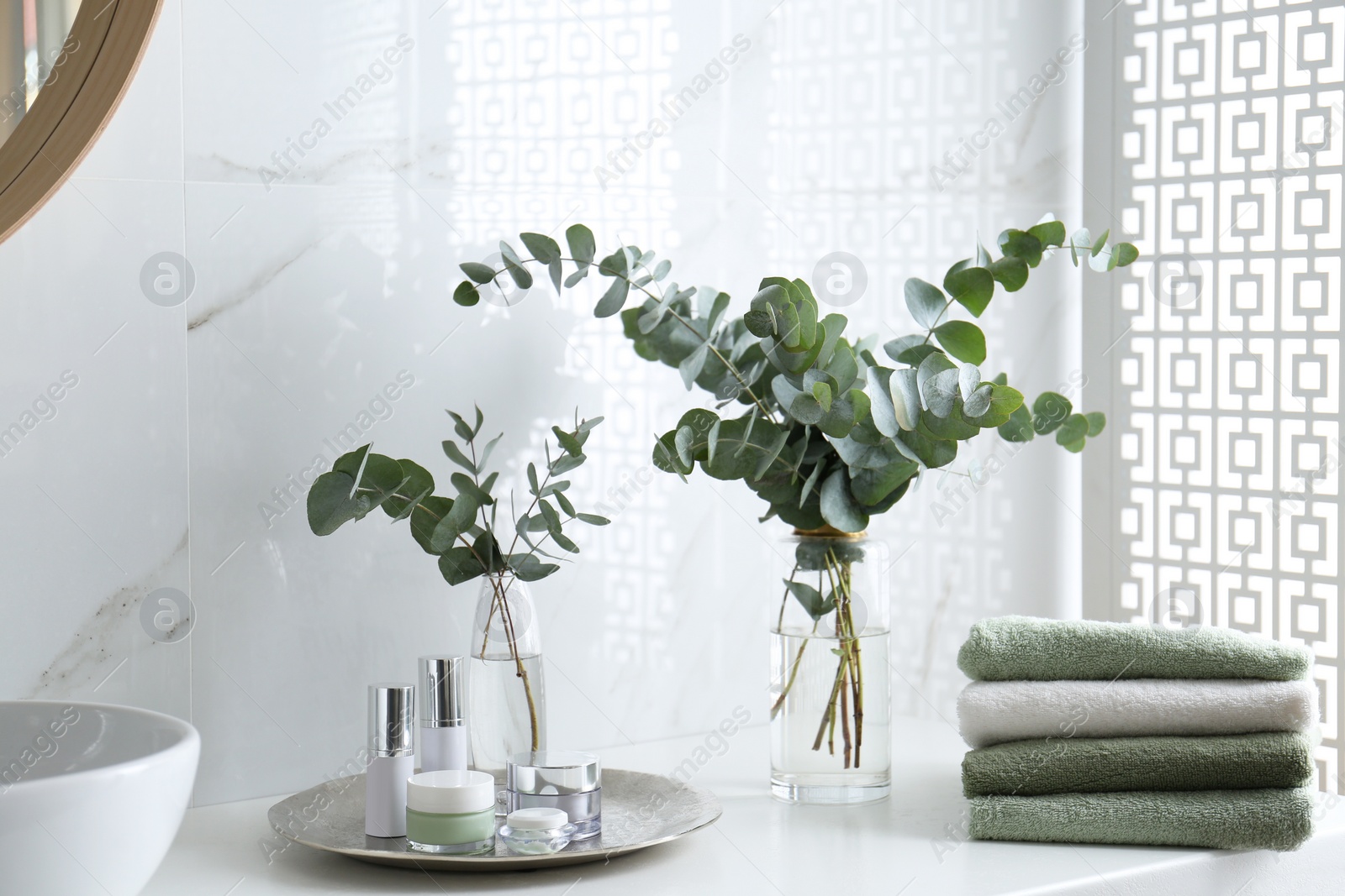 Photo of Fresh eucalyptus branches and cosmetic products on countertop in bathroom