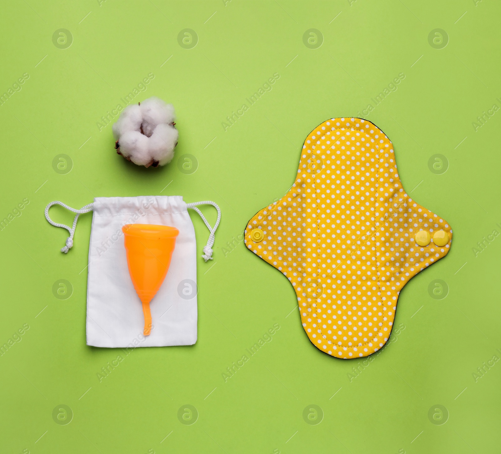 Photo of Reusable cloth pad, menstrual cup and cotton flower on green background, flat lay