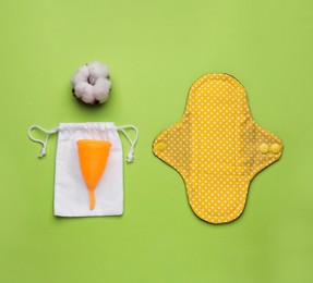 Photo of Reusable cloth pad, menstrual cup and cotton flower on green background, flat lay