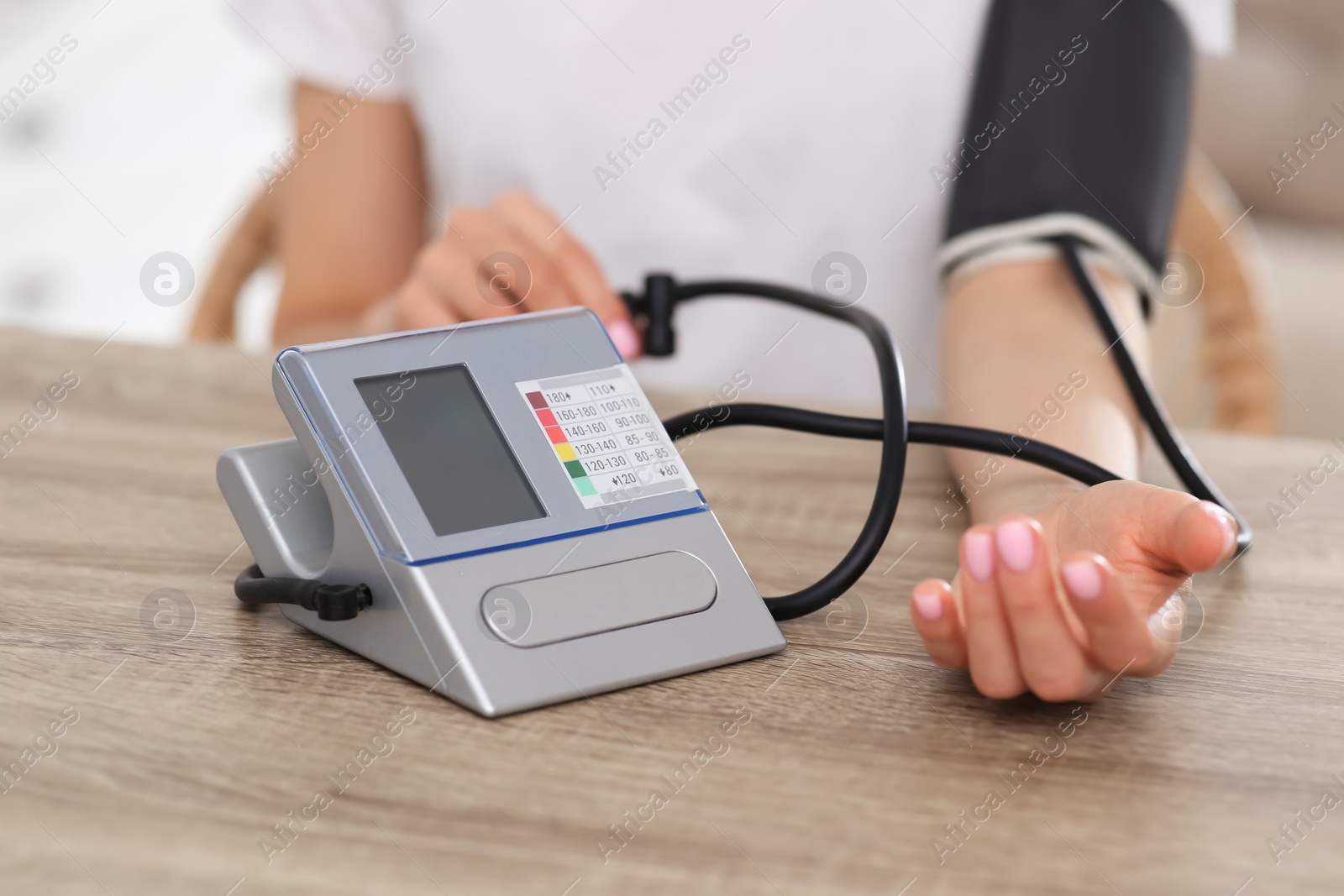 Photo of Woman checking blood pressure at wooden table indoors, closeup