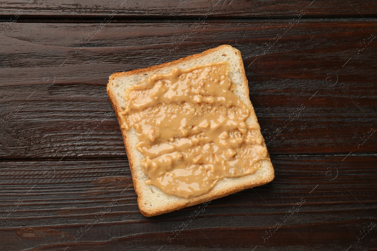 Photo of Delicious toast with peanut butter on wooden table, top view