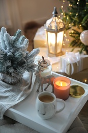 Photo of Cup of cocoa, candle and decorative deer on tray at home. Christmas celebration