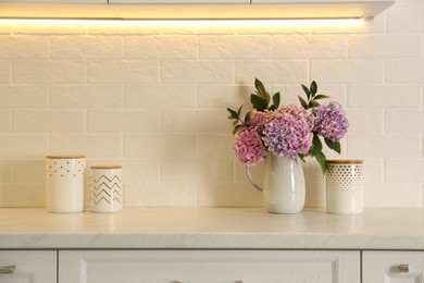 Photo of Bouquet with beautiful purple hydrangea flowers and jars on light countertop